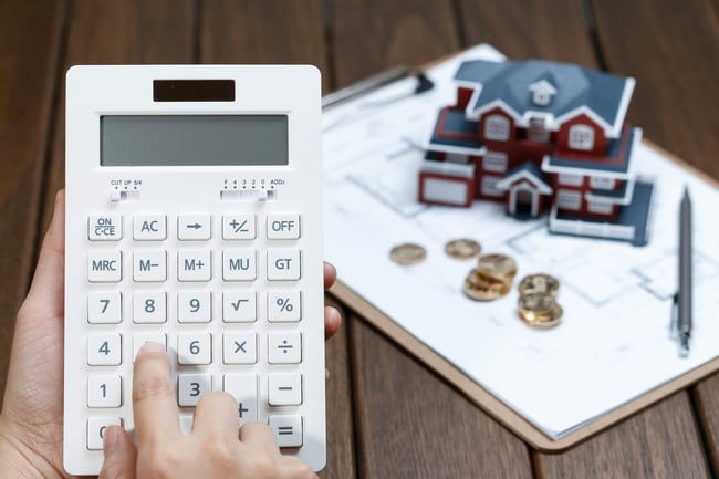a-female-hand-operating-a-calculator-in-front-of-a-villa-house-model-scaled