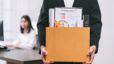 człowiek niesie pudło z dokumentami i przyborami do pracy biurowej