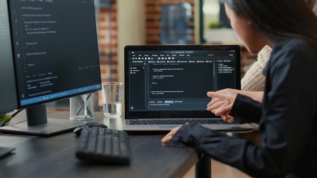 team-of-programmers-talking-about-algorithm-running-on-laptop-screen-pointing-at-source-code-while-sitting-at-desk-software-developers-collaborating-
