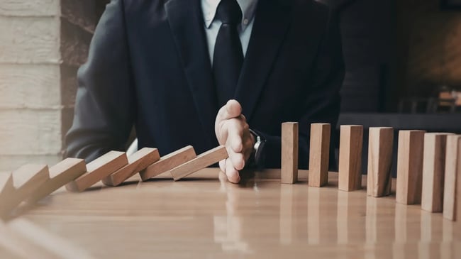 człowiek w garniturze zatrzymuje ręką klocki domino