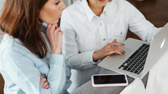 dwie elegancko ubrane kobiety rozmawiają przeglądając laptopa