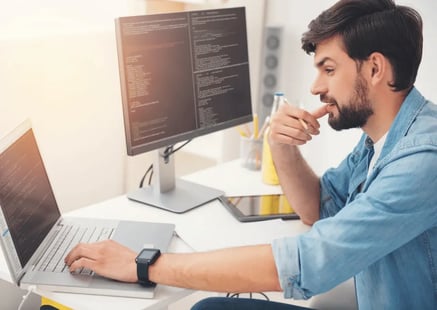 mężczyzna pracuje przy laptopie i monitorze