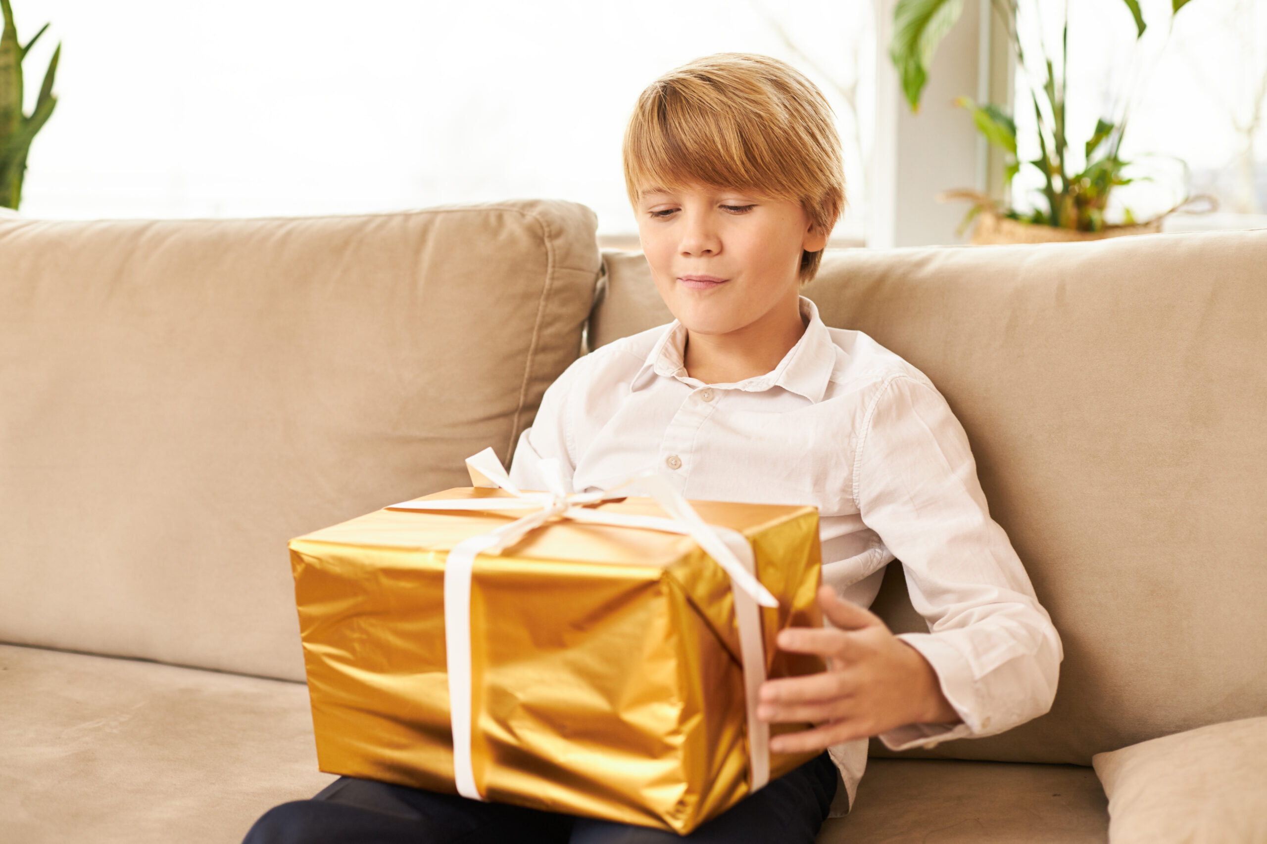 cute-caucasian-teenager-sitting-sofa-with-new-yeara-s-gift-his-lap-handsome-boy-ready-open-golden-box-with-christmas-present-it-having-curious-antici