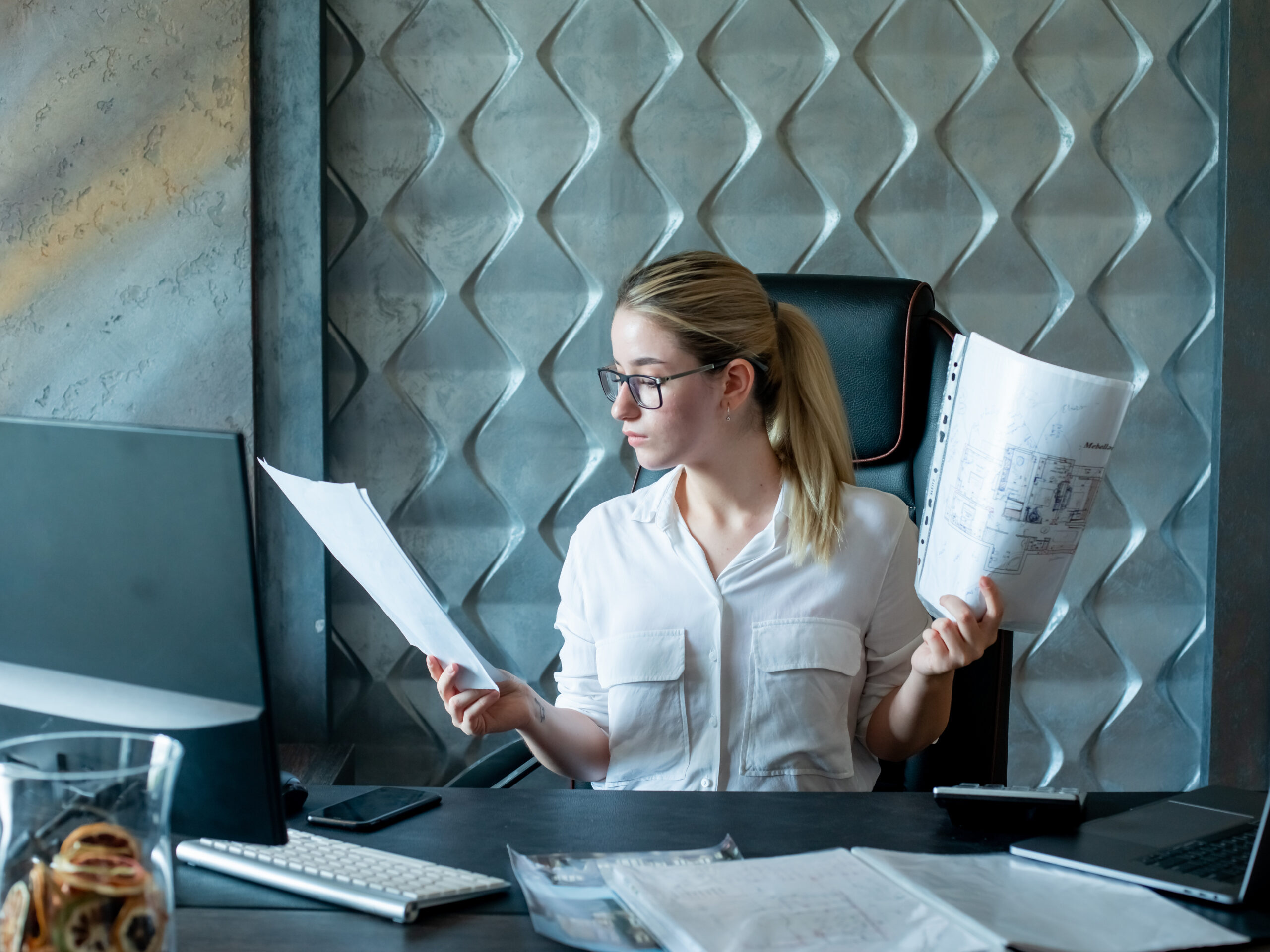 portrait-young-office-worker-woman-sitting-office-desk-with-documents-looking-them-with-serious-confident-expression-face-working-office-scaled