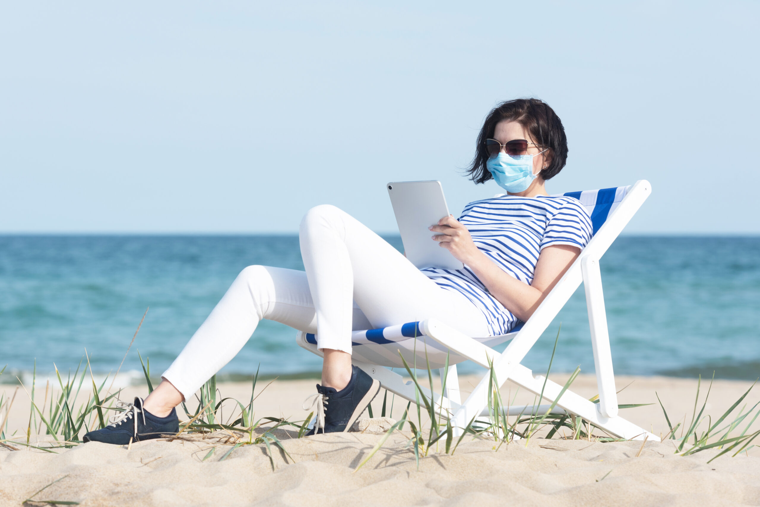 woman-in-a-mask-sitting-with-laptop-on-empty-coast-social-distance-concept-coronavirus-covid19-scaled